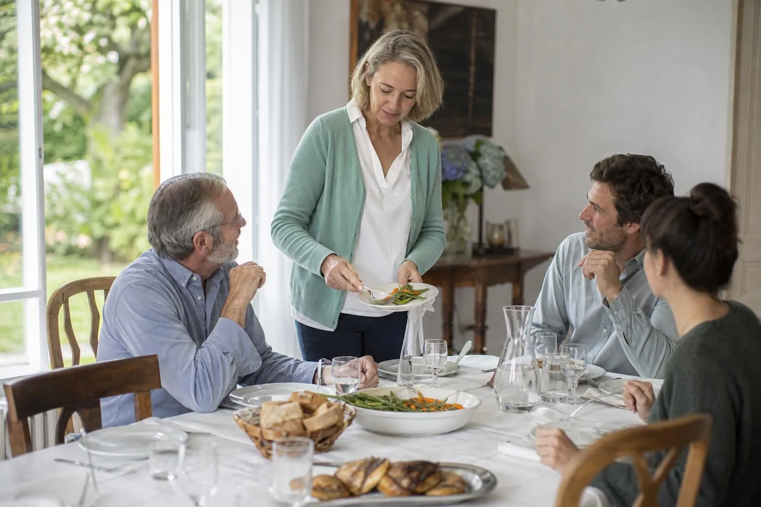 Déjeuner de famille du dimanche autour d’une grande table claire, une femme d’une cinquantaine d’années se servant des légumes dans un plat commun